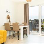Essbereich mit Tisch und Stühlen, gelber Sofa-Ecke und Balkon mit Sitzgelegenheiten.