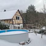 Schneebedeckter Garten mit Pool und Fachwerkhaus im Hintergrund.
