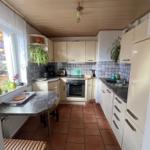 Küche mit Arbeitsplatten, Spüle, Herd und Fenster. Holzdecke und Fliesenboden.