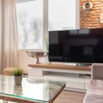 Wohnzimmer mit Fernseher, Glas-Tisch und Holzwand.