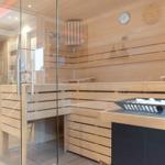 Sauna mit Holzbank und Glaswand. Auf dem Tisch liegen weiße Steine.