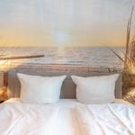 Schlafzimmer mit Bett, Kissen und Wandbild von Strand und Meer.