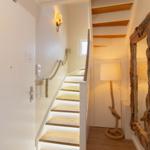 Hausflur mit Treppe, Seilgeländer und grobem Holzspiegel.