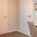 Wohnraum mit Schreibtisch, Stuhl und Wandbild. Zwei Türen und Holzboden.