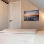 Schlafzimmer mit Bett, Wandbild und Schiebetüren unter Dachschrägen.