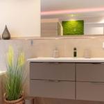 Badezimmer mit Waschbecken, Spiegel und Pflanze.