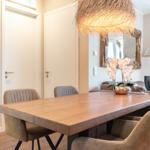 Esszimmer mit Holztisch, Stühlen und Deckenleuchte. Im Hintergrund Wohnzimmer mit Kamin.