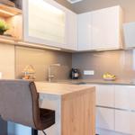 Küche mit Holzinsel, weißen Schränken und Barhockern. Auf der Arbeitsplatte stehen Obst und eine Kaffeemaschine.