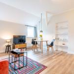 Wohnzimmer mit Sofa, Esstisch und Regal. Holzboden und Fenster sichtbar.