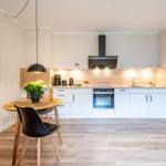 Küche mit Esstisch, weißen Schränken und Holzoptik. Schwarze Deckenleuchte und rote Sitzgelegenheit.