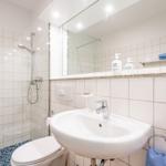 Badezimmer mit Dusche, Waschbecken und Toilette. Weiße Fliesen und Spiegel.