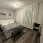 Schlafzimmer mit Bett, Nachttischen, Stuhl und Fenster mit Vorhängen.