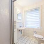 Badezimmer mit Toilette, Waschbecken und Fenster mit Jalousie.