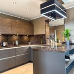 Moderne Küche mit dunklen Schränken, Marmorarbeitsplatte und moderner Beleuchtung.