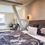 Schlafzimmer mit Bett, Fenster und Wandbeleuchtung. Tapete und Bettwäsche mit floralen Mustern.