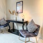 Zwei Sessel mit Kissen stehen um einen schwarzen Tisch herum. An der Wand hängt ein Bild.