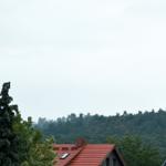 Dach mit roten Ziegeln, umgeben von Bäumen und einem bewölkten Himmel.