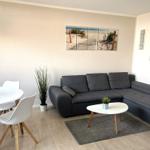 Wohn- und Essbereich mit grauem Sofa, runden Tischen und Wandbildern.