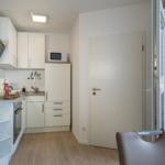 Küche mit weißen Schränken, Herd und Dunstabzug. Tür und Balkon sind sichtbar.