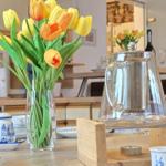 On the table, there is a vase with tulips and a glass kettle on a wooden stand.
