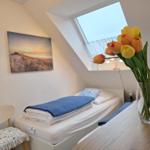 A bedroom with sloped ceilings, bed, chair, and tulips in vase.