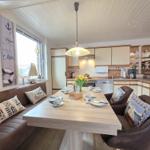 Dining area with kitchenette and window. Wooden table, chairs, cushions, and decor.
