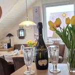 Table with flowers, prosecco, and glasses in dining room with window and beams.