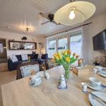 Dining room with table, chairs, and flowers. Living area with sofa and TV in background.