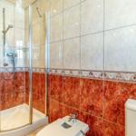 Bad mit Dusche, Toilette und Fliesen in Rot- und Beigetönen.