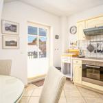 Küche mit Essbereich, Fenster zur Terrasse und Küchenzeile mit Dunstabzug.