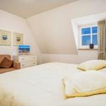 Schlafzimmer mit Bett, Sessel, Schrank und Fenster. Wandbild und Nachttisch sichtbar.