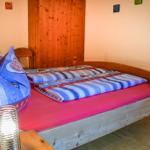 Ein Bett mit Holzrahmen, roter Matratzenauflage und blau-weiß gestreifter Bettwäsche.