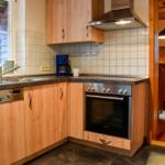 Küche mit Holzschränken, Spüle und Herd. Durchgang zur Essnische mit Holztisch und Stühlen.