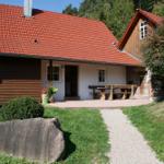 Haus mit rotem Dach, Terrasse und Holztisch. Gras, Steinweg und Bäume umgeben es.