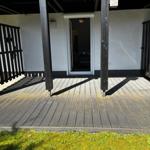 Terrasse mit Holzdielen und schwarzem Zaun, Tür führt in das Haus.