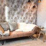 Ein Sofa mit Felldecke und Kissen vor einer gemusterten Wand.