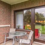 Terrasse mit Tisch, zwei Stühlen und Glaswand. Wandbeleuchtung und rote Ziegelmauer.