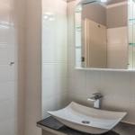 Badezimmer mit Waschbecken, Spiegel und Glasregalen an der Wand.