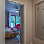 Schlafzimmer mit Bett, rotem Sessel und Blick auf Garten. Flur mit Garderobenwand.