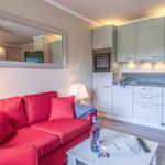 Ein Wohnbereich mit rotem Sofa, Küchenzeile und Spiegel an der Wand.