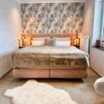 Schlafzimmer mit Bett, Nachttischen und Fenster. Wandtapete und Fellteppich.