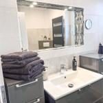 Badezimmer mit Waschbecken, Spiegel und Handtüchern.