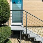 Eingangstreppe mit Metallgeländer und Steinplatten führt zur Haustür.