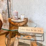 Auf einem Glas-Tisch steht eine Kerze, eine Eule und ein Holzschild mit Schrift.