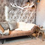 Ein Sofa mit Felldecke und Kissen vor einer gemusterten Wand mit Lichterkette.