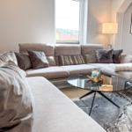 Ein Wohnzimmer mit grauem Sofa, Glas-Tisch und Fensterblick.