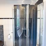 Duschkabine mit Glaswand und Duschbrause. Toilette und WC mit Wandhalterung.