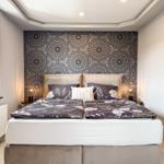 Schlafzimmer mit Doppelbett, gemusterter Wand und Nachttischen mit Lampen.