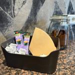 Kaffee- und Zuckertütchen in einem Behälter auf der Arbeitsfläche.