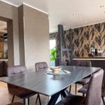 Esszimmer mit dunklem Tisch, Stühlen und Wandtapete mit Blattmuster.